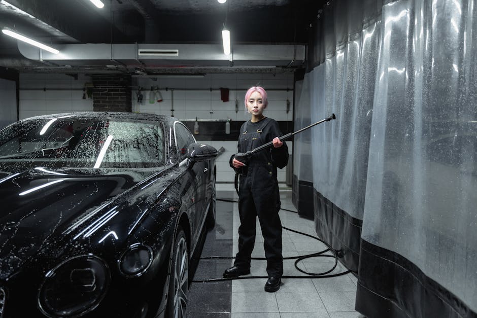 A woman using a pressure washer to clean a black sports car at an indoor car wash facility.
